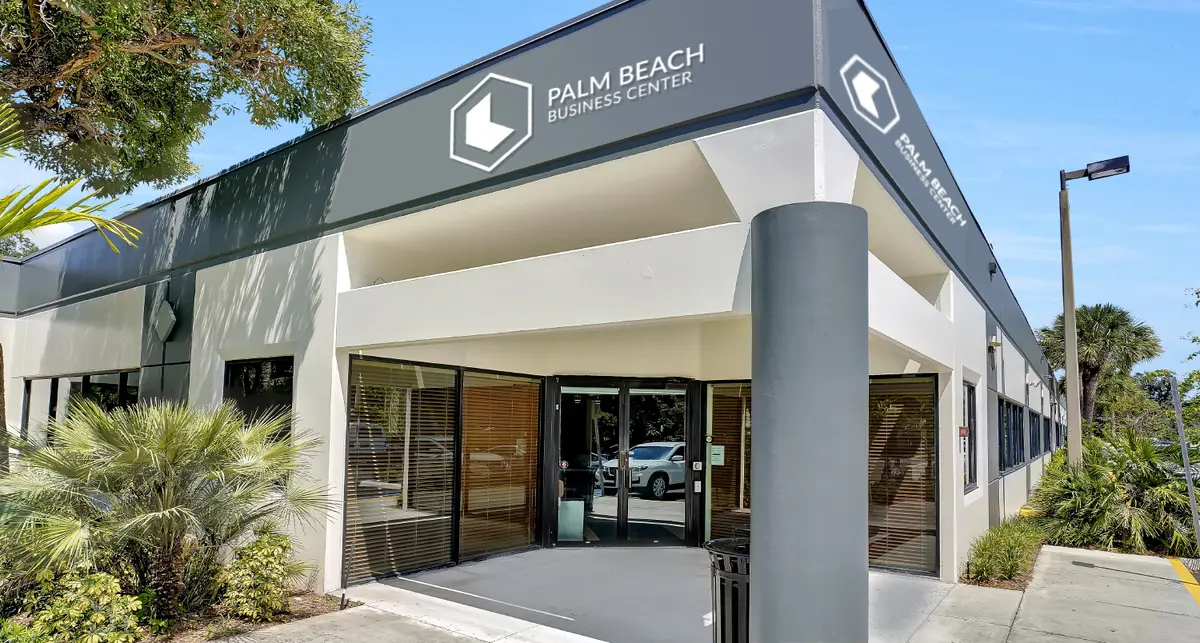 A white one story concrete building with gray roof and pillar accents with the sign reading Palm Beach Business Center