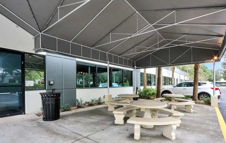 A large covered patio with three concrete circular tables that are accompanied by three curved concrete benches at each of them.